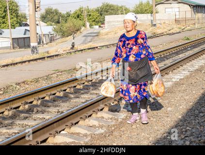 Frauen in traditioneller Kleidung, die auf den Schienen laufen, um Rundbrot (Lepeshka), Kyzyl-Orda, Kasachstan, Zentralasien zu verkaufen Stockfoto