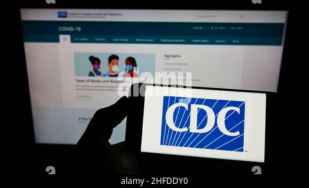 Person, die das Smartphone mit dem Logo der Centers for Disease Control and Prevention (CDC) auf dem Bildschirm vor der Website hält. Konzentrieren Sie sich auf die Telefonanzeige. Stockfoto