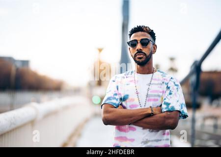 Porträt eines afroamerikanischen Mannes in buntem T-Shirt und Sonnenbrille mit gekreuzten Armen Stockfoto