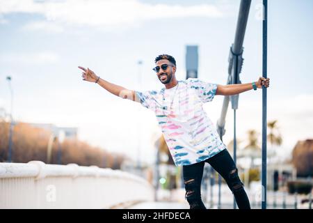 Lächelnder schwarzer Mann in Sonnenbrille erfreut sich auf der Straße, die Arme zu heben Stockfoto