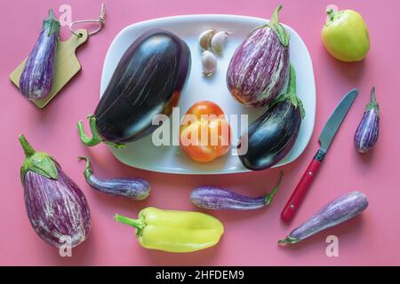 Verschiedene Gemüse - Auberginen und Paprika - auf rosa Hintergrund. Flach liegend Stockfoto
