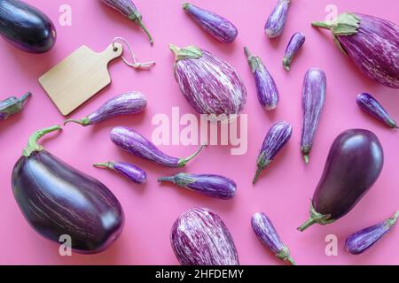 Verschiedene Sorten Auberginen und Schneidebrett auf rosa Hintergrund Stockfoto