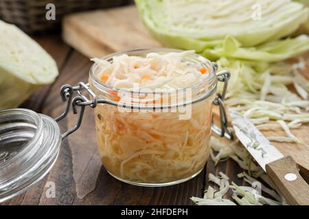 Krug mit saurem Kohl, eingelegtem Sauerkraut. Fermentierter Kohl, Krautsalat. Gehackter Kohl auf einem Schneidebrett für die Herstellung von Sauerkraut auf dem Hintergrund. Er Stockfoto