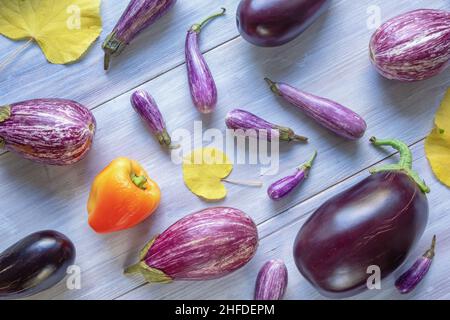 Herbstgemüse. Roter Paprika, verschiedene Auberginen-Sorten und gelbe Blätter auf weißem rustikalem Tisch Stockfoto