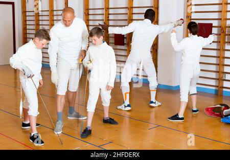 Fokussierte Jungen fechten aufmerksam dem professionellen Fechttrainer im Fitnessstudio zu Stockfoto