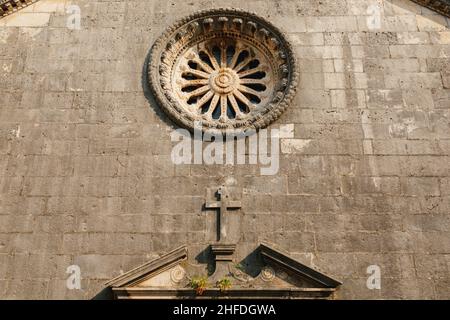 Rosenfenster mit Ornamenten an der dunklen Steinmauer der Kirche über dem Eingang Stockfoto