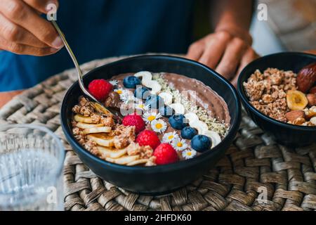 Vogelansicht einer veganen Schokoladen-Smoothie-Schüssel mit Früchten und Müsli wie knusprigen Hafer, Beeren und Nüssen für ein gesundes Frühstück Stockfoto