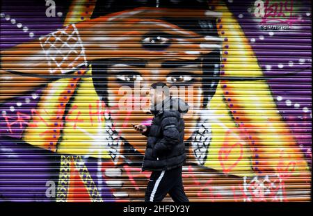 London, Großbritannien. 16th Januar 2022. Ein Mann geht in der Brick Lane in London, Großbritannien, am 15. Januar, an Graffiti vorbei. 2022. Im Osten Londons ist die Brick Lane berühmt für ihre Street Art. Quelle: Li Ying/Xinhua/Alamy Live News Stockfoto