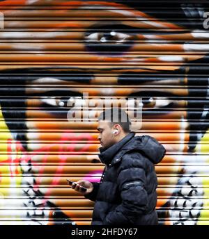 London, Großbritannien. 16th Januar 2022. Ein Mann geht in der Brick Lane in London, Großbritannien, am 15. Januar, an Graffiti vorbei. 2022. Im Osten Londons ist die Brick Lane berühmt für ihre Street Art. Quelle: Li Ying/Xinhua/Alamy Live News Stockfoto