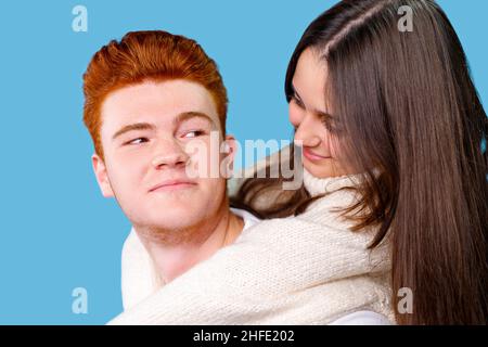 Nahaufnahme eines Rothaarboyfriend und seiner brünetten Freundin, die sich angucken, hält er sie auf dem Rücken und lächelt. Stockfoto