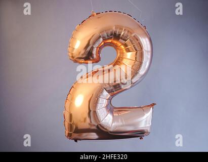 Berlin, Deutschland. 14th Januar 2022. ABBILDUNG - Ein goldener Ballon in Form der Zahl 2 hängt vor einem grauen Hintergrund. (Posierte Szene) im Februar dieses Jahres gibt es mehrere Tage, die für ein besonderes Hochzeitsdatum geeignet sind, darunter die Alkoholzahlendaten, d.h. 2.2.22 und 22,2.22. Quelle: Annette Riedl/dpa/Alamy Live News Stockfoto