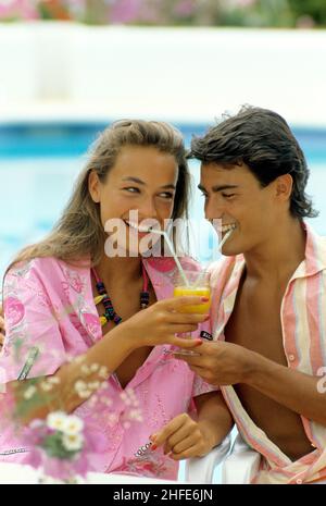 Liebevolle junge Paar lächelnd glücklich aussehen Front Kamera Porträt trinken Orangensaft coktail auf gleichen Glas Sommerferien Hintergrund Pool Stockfoto