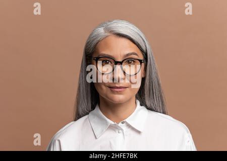Porträt einer fröhlichen positiven Geschäftsfrau im weißen Hemd lächelnd zur Kamera, zufrieden mit dem Leben, charismatische Individualität. Innenaufnahme des Studios auf beigefarbenem Hintergrund Stockfoto