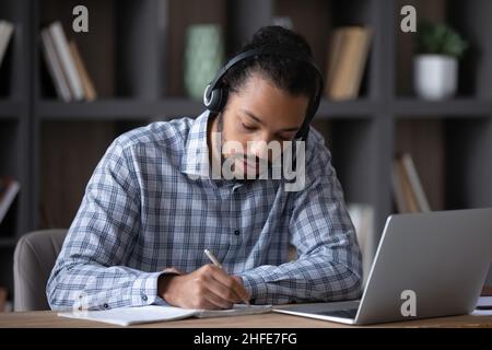 Fokussierter Schüler mit Kopfhörern und Mikrofon, der Notizen schreibt Stockfoto