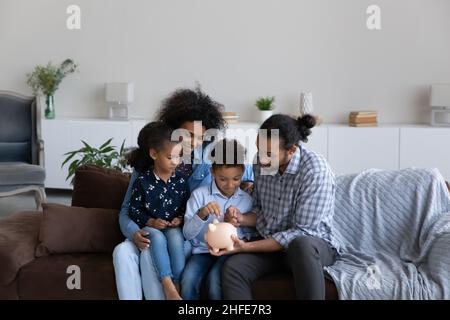 Glückliche afroamerikanische Eltern, die Geschwisterkinder lehren, Geld zu sparen Stockfoto