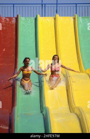 2 junge Frauen slidng auf farbigen Rodel frohe Feiertage lustigen Look Stockfoto