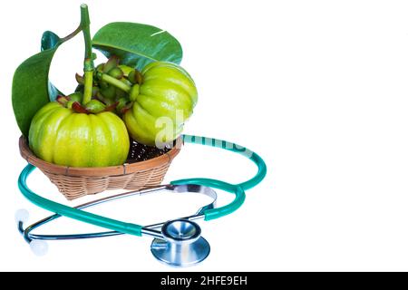 Nahaufnahme Stillleben garcinia atroviridis frisches Obst auf Holzkorb und Stethoskop auf weißem Hintergrund. Kräutersauer schmeckt viel Vitamin C für gutes h Stockfoto