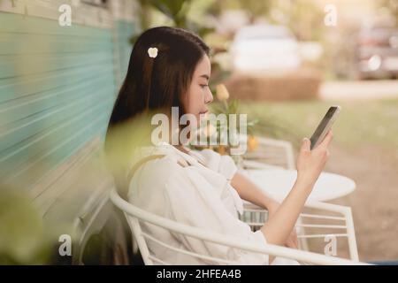 Asiatische Dame im Freien sitzen entspannen Blick auf Smartphone Fühlen Sie sich Freizeit im Urlaub Stockfoto