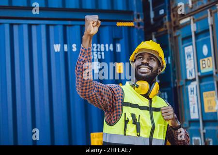 Afrikanisch Schwarze Mitarbeiter glücklich lächeln steigende Hand in Fracht Versand logistischen Hafen zu kämpfen. Stockfoto