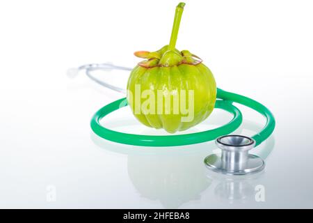 Garcinia cambogia frisches Obst und Stethoskop mit Reflexion, isoliert auf weiß. Garcinia atroviridis ist eine Gewürzpflanze mit hohem Vitamin-C- und Hydroxiveaus Stockfoto