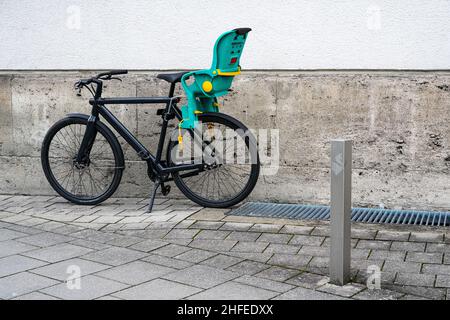 Schwarzes Fahrrad mit grünem Kindersitz auf einem Bürgersteig an einer Hauswand. Stockfoto