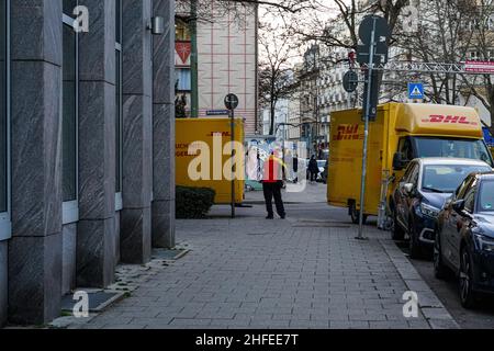 Zwei DHL Paketzustellwagen an einer Kreuzung. Zwischen den beiden ein DHL-Kurierlieferer. Stockfoto