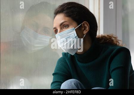 Nachdenkliche unglückliche junge Frau in Gesichtsmaske fühlt sich einsam. Stockfoto