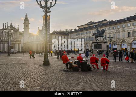 Hintergrundansicht einer kleinen Band, die als Weihnachtsmann gekleidet ist und Weihnachtslieder auf der Piazza San Carlo bei Sonnenuntergang, Turin, Piemont, Italien, spielt Stockfoto