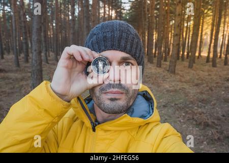 Ein Mann hält in der Natur einen Kompass über sein rechtes Auge. Konzept von Suchen und Orientierung Stockfoto