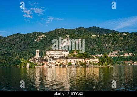 Die Insel St. Julius mit der Basilica di San Giulio auf der anderen Seite des Orta-Sees, umgeben von Bergen in der Ferne. Stockfoto