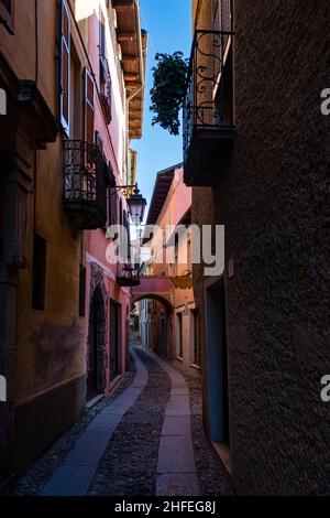 Eine kleine, schmale Gasse in Orta San Giulio mit Toren, Hausfassaden und Balkonen, gepflastert mit Kopfsteinpflaster. Stockfoto