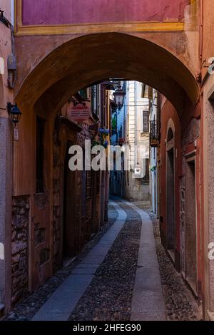 Eine kleine, schmale Gasse in Orta San Giulio mit Toren, Hausfassaden und Balkonen, gepflastert mit Kopfsteinpflaster. Stockfoto