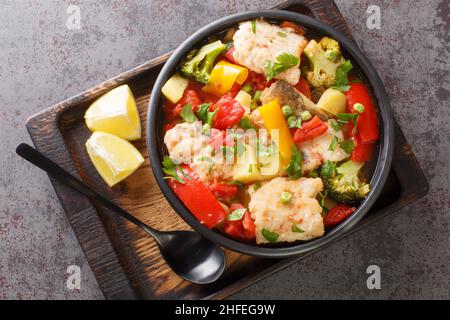Fischeintopf mit Paprika, Kartoffeln, Erbsen, Zwiebeln, Brokkoli und Tomaten aus nächster Nähe in einer Schüssel auf dem Tisch. Horizontale Ansicht von oben Stockfoto