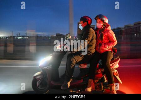 (220116) -- YUTIAN, 16. Januar 2022 (Xinhua) -- Abudulezizi Maisedi, der seine Frau Maynurhan Amang (R) mit einem Elektrofahrrad trägt, wird auf dem Weg zur Arbeit im Tianjin Industriepark im Yutian County, nordwestlich der Autonomen Region Xinjiang Uygur, gesehen, 14. Januar 2022. Yutian County, einst ein von Armut gebeuteltes Gebiet in Xinjiang, hat die Entwicklung arbeitsintensiver Industrien wie Textil-, Bekleidungs- und Sockenherstellung verstärkt. Im Tianjin Industriepark in Yutian wurde am 1. Januar 2022 eine Produktionsbasis der chinesischen Sportmarke Erke in Betrieb genommen, die mehr als 500 Arbeitsplätze für Einheimische bot. M Stockfoto