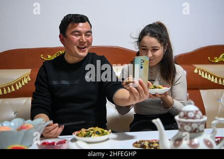 (220116) -- YUTIAN, 16. Januar 2022 (Xinhua) -- Maynurhan Amang (R) und Abudulezizi Maisedi unterhalten sich mit Familienmitgliedern in ihrer Wohnung im Tianjin Industriepark im Yutian County, nordwestlich der Autonomen Region Xinjiang Uygur in China, 13. Januar 2022. Yutian County, einst ein von Armut gebeuteltes Gebiet in Xinjiang, hat die Entwicklung arbeitsintensiver Industrien wie Textil-, Bekleidungs- und Sockenherstellung verstärkt. Im Tianjin Industriepark in Yutian wurde am 1. Januar 2022 eine Produktionsbasis der chinesischen Sportmarke Erke in Betrieb genommen, die mehr als 500 Arbeitsplätze für Einheimische bot. Maynurh Stockfoto