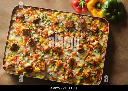 Hausgemachte Pizza mit Paneer, Mozzarella-Käse, rot-gelb-grünen Kapsikken und Zwiebeln. Gebacken in einem rechteckigen Tablett Stockfoto