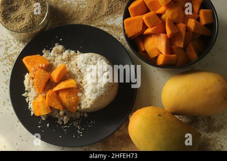 Gedünsteter Hirsemehlkuchen oder hirseputtu mit Mangoscheiben und Kochbananen. Eine Vielzahl von Kerala Reis Dampfkuchen mit Scheckenhof Stockfoto