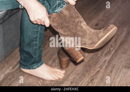 Nahaufnahme. Schuhmontage. Weibliche Hände ziehen einen Stiefel auf ein Bein. Das Mädchen zieht Schuhe an. Konzept des Kaufens, des Versuchs an Schuhen und Stiefeln. Stockfoto