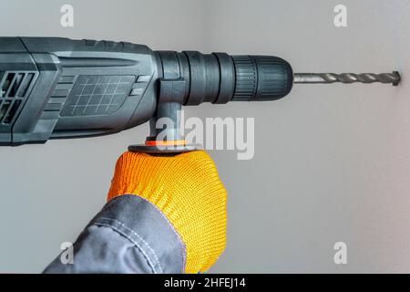 Arbeiter Hand mit einem Bohrhammer. Hände in Schutzhandschuhen mit Hammerbohrer-Perforator. Nahaufnahme Stockfoto