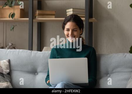 Glückliche junge Freiberuflerin, die zu Hause am Computer arbeitet. Stockfoto