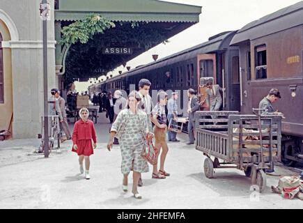 Die Passagiere steigen um 1960 aus einem Zug am Bahnhof Assisi, Assisi, Umbrien, Italien, aus. Post (poste) wird auch mit der Bahn mit Taschen auf einem Handwagen (rechts) transportiert. Der Bahnhof von Assisi befindet sich an der Piazza Dante Alighieri, Santa Maria degli Angeli, etwa 5 Kilometer südwestlich des Stadtzentrums. Der Bahnhof wurde 1866 eröffnet und ist Teil der Bahn Foligno-Terontola, die auch Florenz mit Rom verbindet. Dieses Bild stammt von einem alten Amateur 35mm Farbtransparenz – ein Vintage 1950/60s Foto. Stockfoto