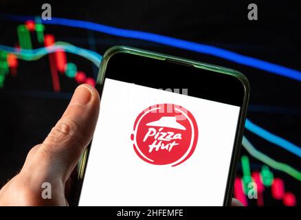 In dieser Fotolabbildung ist das Logo der amerikanischen Fast-Food-Pizza-Restaurantkette Pizza Hut auf einem Smartphone mit einem Index der wirtschaftlichen Börse im Hintergrund zu sehen. Stockfoto