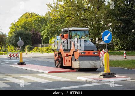 Reparatur der Straße und der Eisbahn legt Asphalt. Ein Straßenbauarbeiter auf einer Eisbahn rollt die Straße. Autobahn Baustelle Landschaft Stockfoto