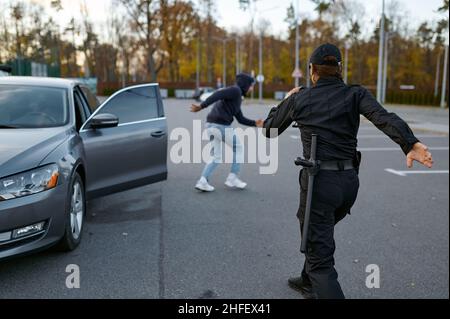 Frau Polizist läuft hinter einem Autodieb mit Kapuze her Stockfoto