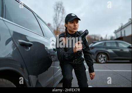 Polizeifrau mit Zielpistole, die in der Nähe des Autos steht Stockfoto