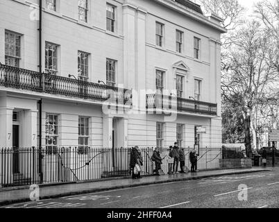 Das Gebäude im georgianischen Stil aus dem 19th. Jahrhundert befindet sich am St. Leonard’s Place in York. Eine Schlange von Leuten wartet an einer Bushaltestelle. Bäume fangen das Sonnenlicht ein. Stockfoto