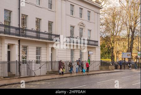 Das Gebäude im georgianischen Stil aus dem 19th. Jahrhundert befindet sich am St. Leonard’s Place in York. Eine Schlange von Leuten wartet an einer Bushaltestelle. Bäume fangen das Sonnenlicht ein. Stockfoto