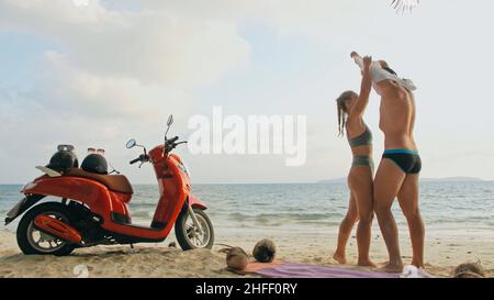 Motorroller Road Trip. Schönes Paar auf rotem Motorrad in weißen Kleidern am Sandstrand. Menschen, die in der Nähe der tropischen Palmen, Meer. Motorradmiete. Stockfoto