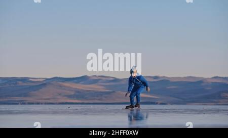 Das Kind trainiert auf Eisschnelllauf. Das Mädchen Schlittschuhe im Winter in Sportbekleidung, Sportbrille, Anzug. Zeitlupe im Freien. Stockfoto