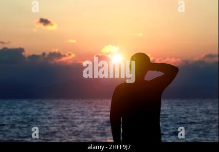 Rückansicht Silhouette Foto von depressiven Mann beobachten den Sonnenuntergang auf dem Meer. Durchdachtes, überdenkliches, nachdenkliches und zukünftiges Plankonzept. Stockfoto